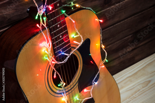 Acoustic guitar in a New Year's garland, guitar in a garland under a wooden wall