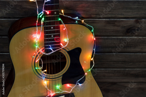 Acoustic guitar in a New Year's garland, guitar in a garland under a wooden wall, copy spaсe
