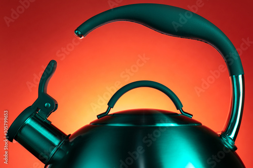 Close-up photo of stainless steel kettle in neon light over red background.