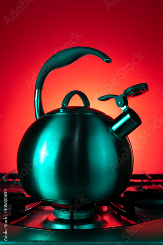 Photo of stainless steel kettle in neon light over red background.