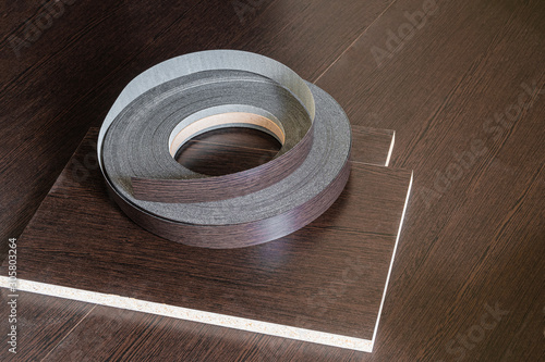 Edging tape lying on laminated chipboard sheets wenge color. Roll melamine edge for finishing of furniture. photo