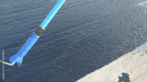 Waterproofing coating. Worker applies bitumen mastic on the foundation. Roofer cover the rooftop polymer modified bitumen waterproofing primer, with a roller brush.