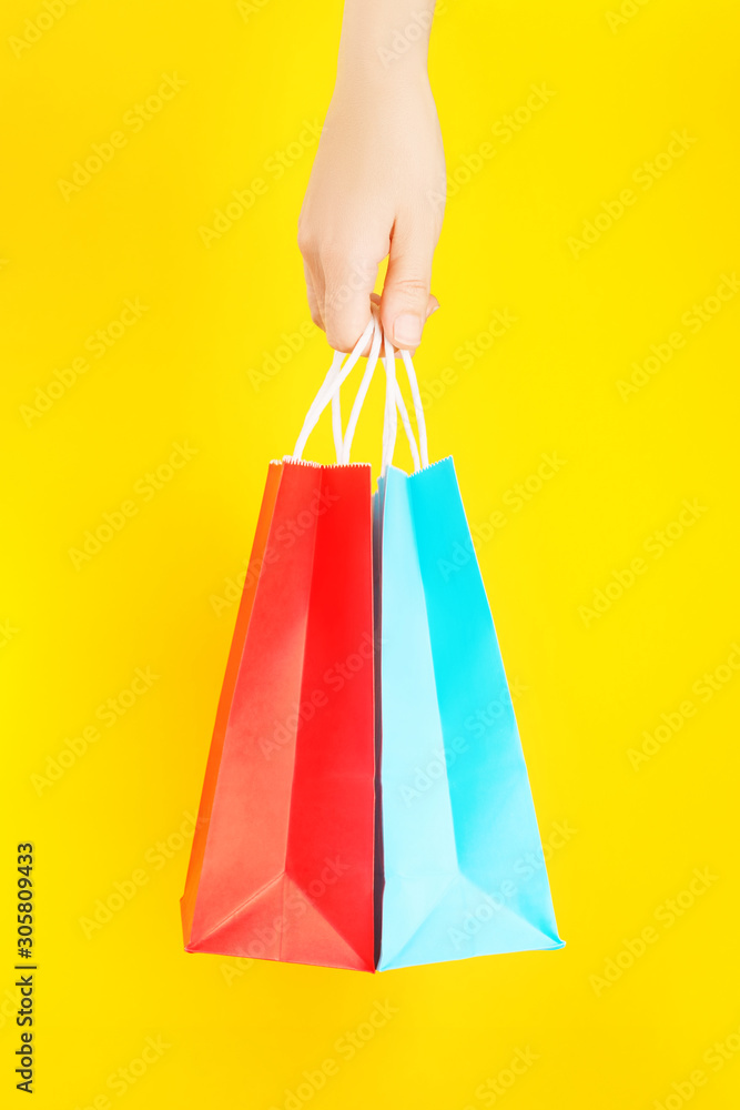 Hand holding red and blue shopping or gift bag against yellow background. The concept of shopping or gifts.