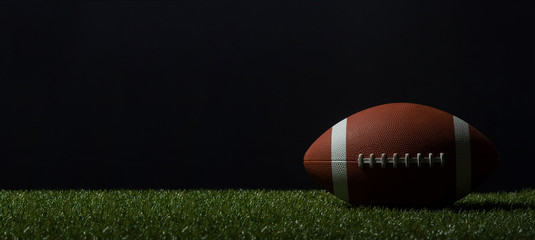 American football on green grass, on black background.