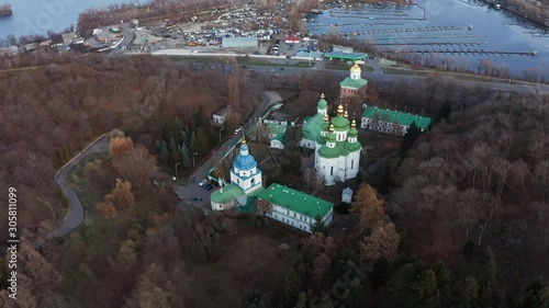 Quadrocopter flight over Vydubychi monastery with copper green roof, church bell towers and gold domes. Vydubychi Monastery with its main temple, refectory and bell tower among the trees in autumn. photo