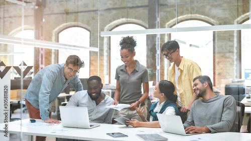 Busy working day. Group of business people communicating with each other and discussing project results while sitting together behind the glass wall in the creative office