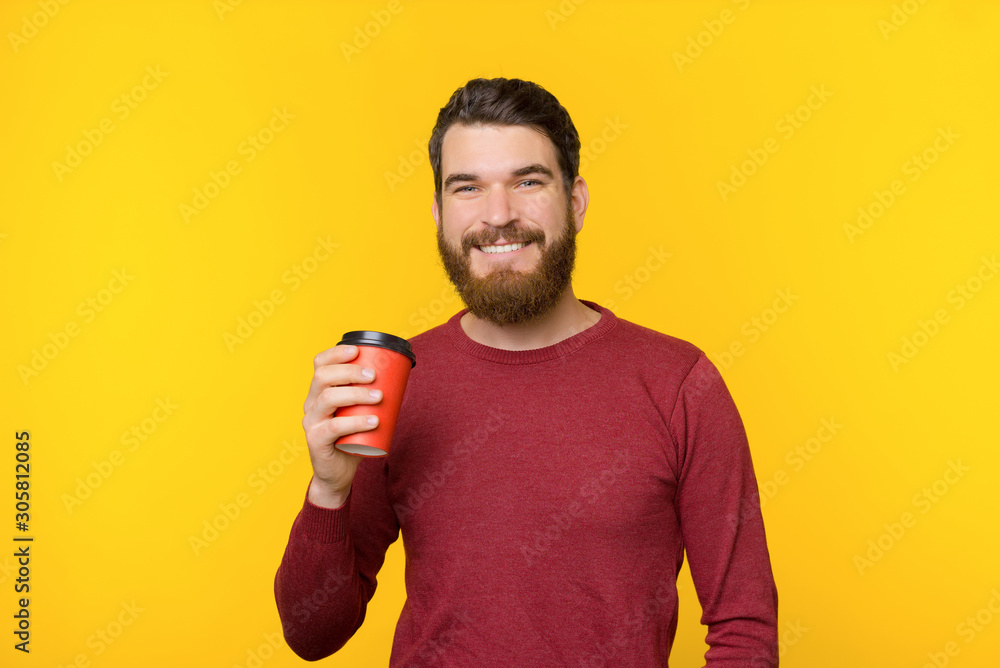 Bearded man smiling and holding a cup of hot drink on yellow background. Bearded man smiling and holding a cup of hot drink on yellow background.