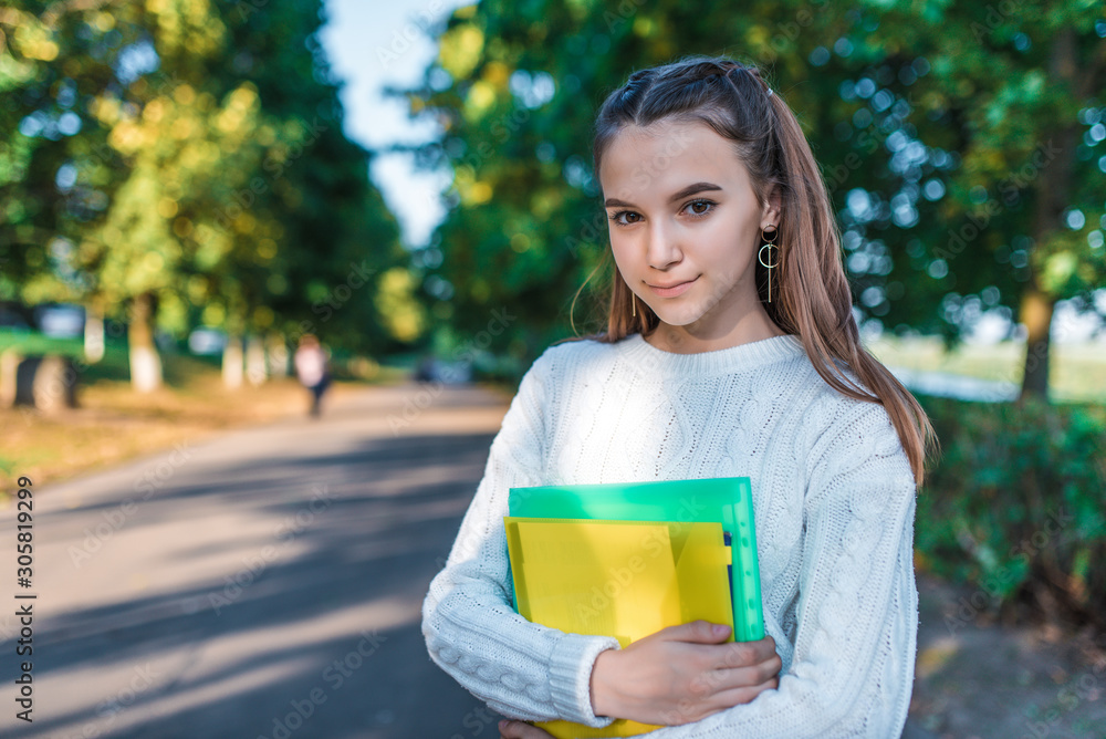 Fototapeta premium teenager girl summer city park, hands holding notebooks notes. Happy smiling posing. Free space for copy text. Concept of rest after lessons school and college, education and acquisition knowledge.