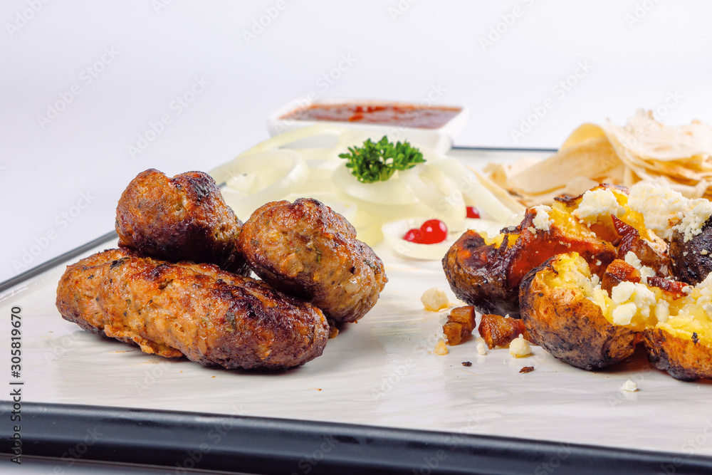 kebab and baked potato with cheese. onion circles and pita bread, red sauce on a white board. great snack dish for beer. close up view kebab and baked potato with cheese. onion circles and pita bread, red sauce on a white board. great snack dish for beer. close up view