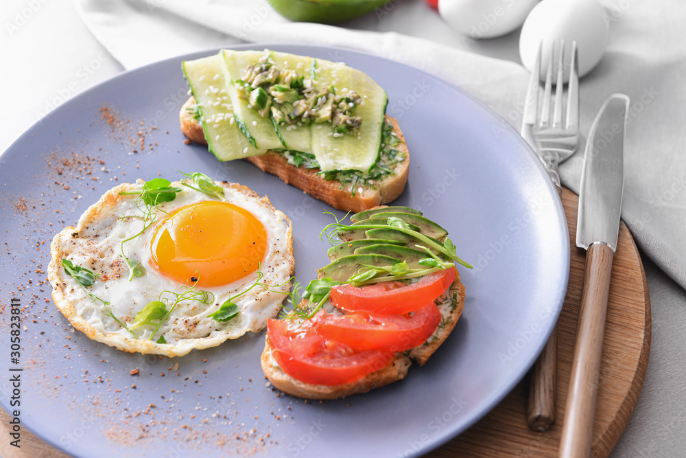 Plate with tasty avocado sandwiches and fried egg on table