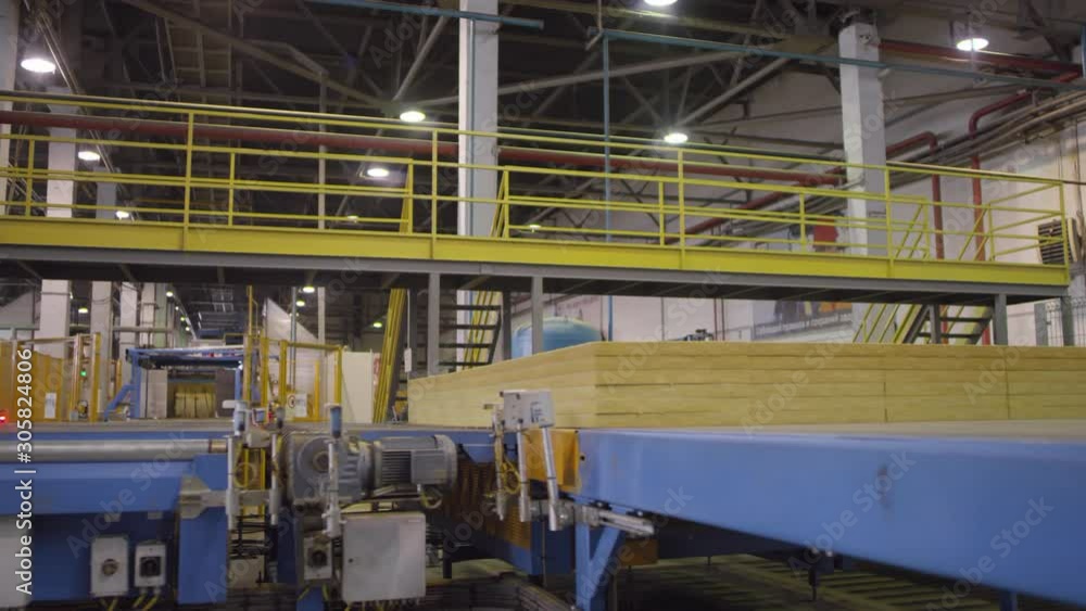 Full tracking shot of stacked slabs of finished mineral wool produce moving along on automated conveyor belt at empty manufacturing plant Full tracking shot of stacked slabs of finished mineral wool produce moving along on automated conveyor belt at empty manufacturing plant