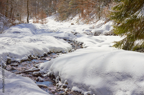 River meandering through snow on a sunny day, during a hiking trip in Bucegi mountains, Romania, in Winter.