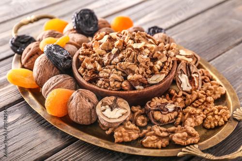 Tray with tasty walnuts and dried fruits on wooden background