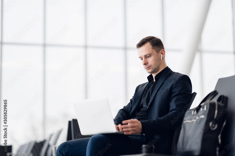 Man with suitcase sitting in airport waiting area while listening music using airpods Man with suitcase sitting in airport waiting area while listening music using airpods