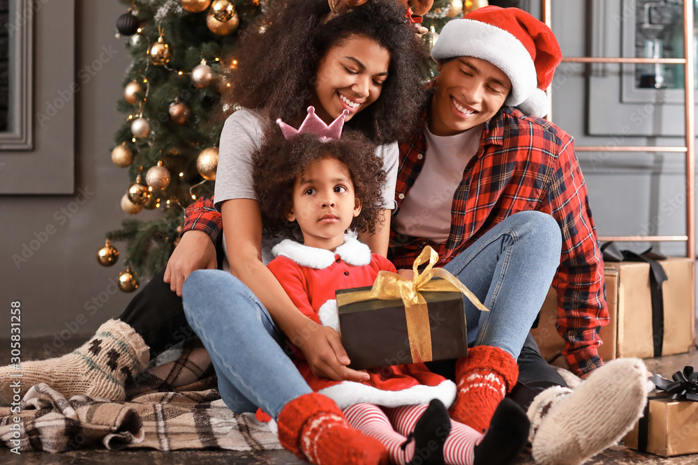 Happy African-American family with gift at home on Christmas eve