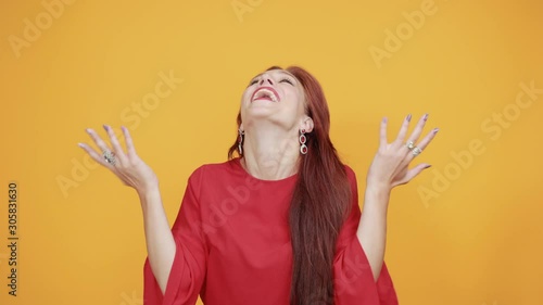 Young woman standing over isolated orange background very happy and excited fluffing hair, keeping thumbs up with arms raised, smiling for success, closed eyes.