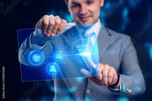 Business, technology, internet and networking concept. Young businessman working on his laptop select the icon action plan on the virtual display.