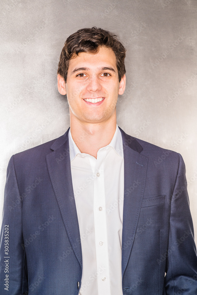 Portrait of Young Handsome Businessman in New York City. Young happy college student wearing blue suit, white shirt, standing against silver metal background, smiling. Close Up. Head Shot..