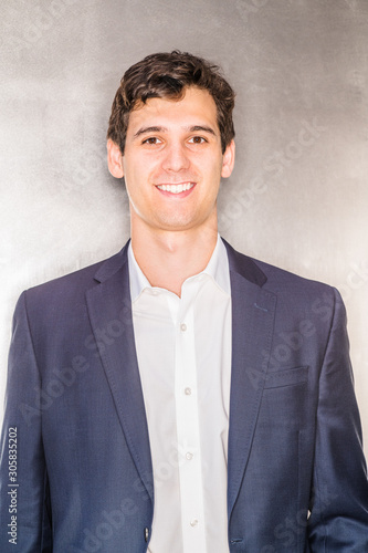 Obraz na płótnie Portrait of Young Handsome Businessman in New York City. Young happy college student wearing blue suit, white shirt, standing against silver metal background, smiling. Close Up. Head Shot.. w salonie