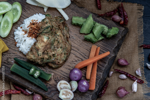 A local Thai food style, Fried acacia pennata omelet or cha-om eggs on jasmine rice with the ingredient and fresh vegetables on a wooden background, Thai Cuisine.