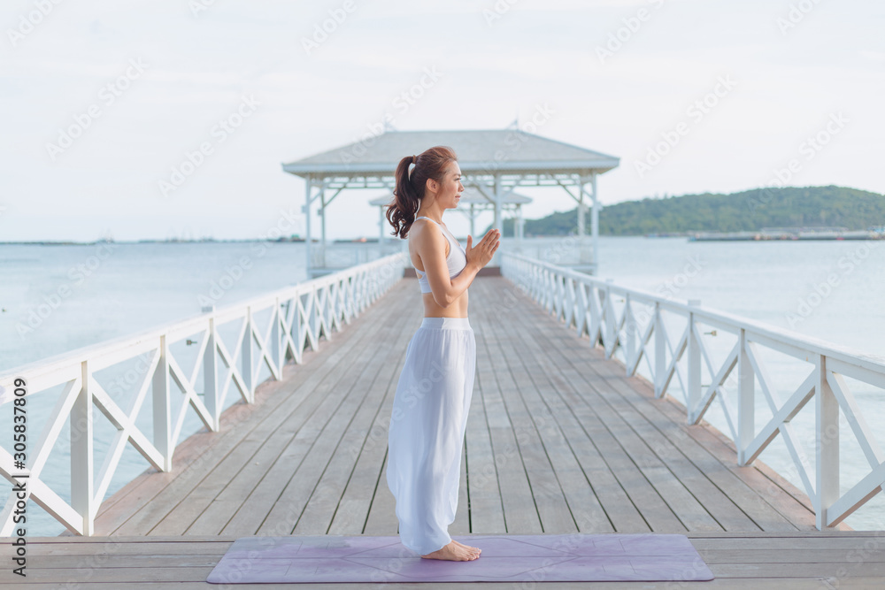 Young women doing yoga, practicing yoga postures on the white bridge range Yoga landscape Beautiful sky and enjoying the sea view On the concept of exercise, health care