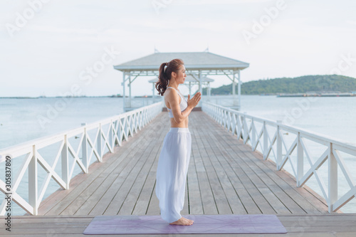 Young women doing yoga, practicing yoga postures on the white bridge range Yoga landscape Beautiful sky and enjoying the sea view On the concept of exercise, health care