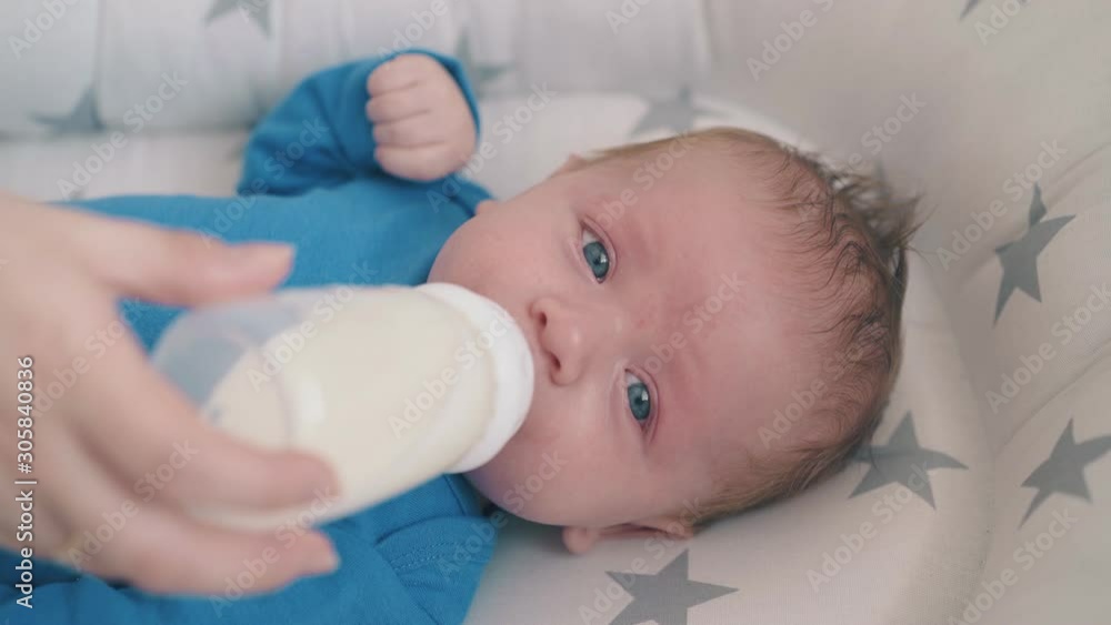 upset little boy with blue eyes eats fresh milk mix with mother help lying in soft sleeping cocoon at home upset little boy with blue eyes eats fresh milk mix with mother help lying in soft sleeping cocoon at home