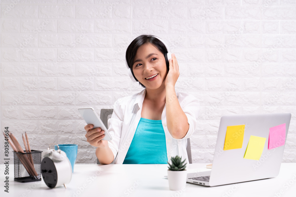 Obraz premium Happy woman with headphones listening music from smart phone at office