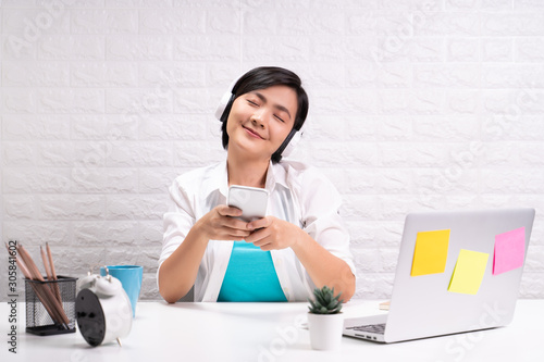 Happy woman with headphones listening music from smart phone at office