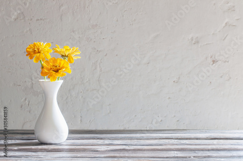 yellow zinnia in white vase on wooden table