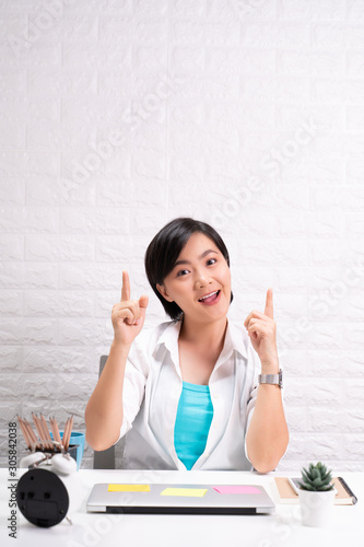 Happy woman sitting at home office and pointing to copy space