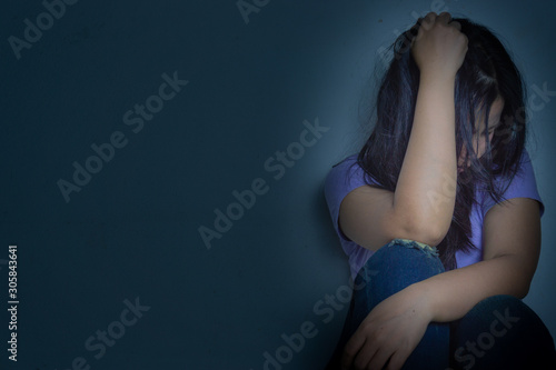 sad woman hug her knee and cry sitting alone in a dark room. Depression, unhappy, stressed and anxiety disorder concept © saran