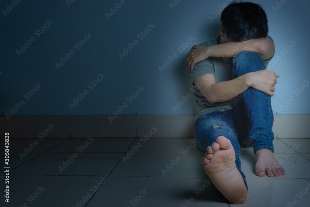 Fototapeta premium sad man hug his knee and cry sitting alone in a dark room. Depression, unhappy, stressed and anxiety disorder concept