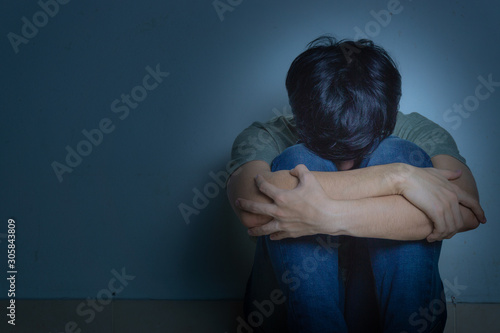 sad man hug his knee and cry sitting alone in a dark room. Depression, unhappy, stressed and anxiety disorder concept