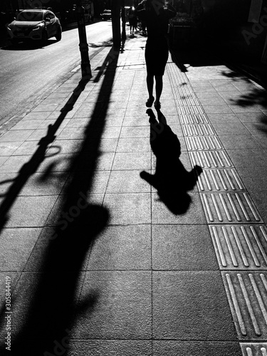 Black and white silhouette shadow of woman in busy and rush walking on the street to go to work in the morning with strong sun light.