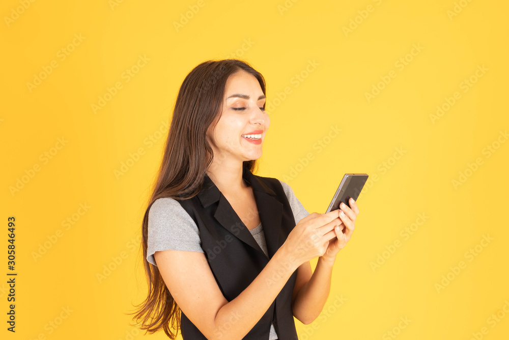A woman standing and playing with a mobile phone In the yellow background A woman standing and playing with a mobile phone In the yellow background