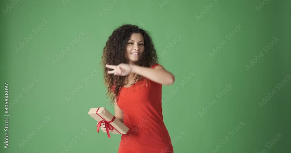Joyful woman holding Christmas present and dancing over green background Joyful woman holding Christmas present and dancing over green background