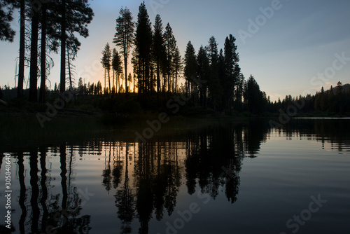 Trees in silhouette at sunset reflected in still water of mountain lake