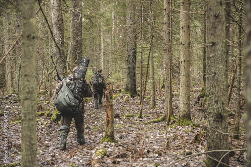 two men, in camouflage, hunters, walk in a dense forest, looking for prey, with weapons