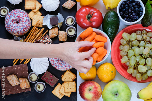 Fototapeta Naklejka Na Ścianę i Meble -  Healthy and unhealthy food concept, fruits and vegetables vs donuts, sweets and chocolate with woman's hand. Top view