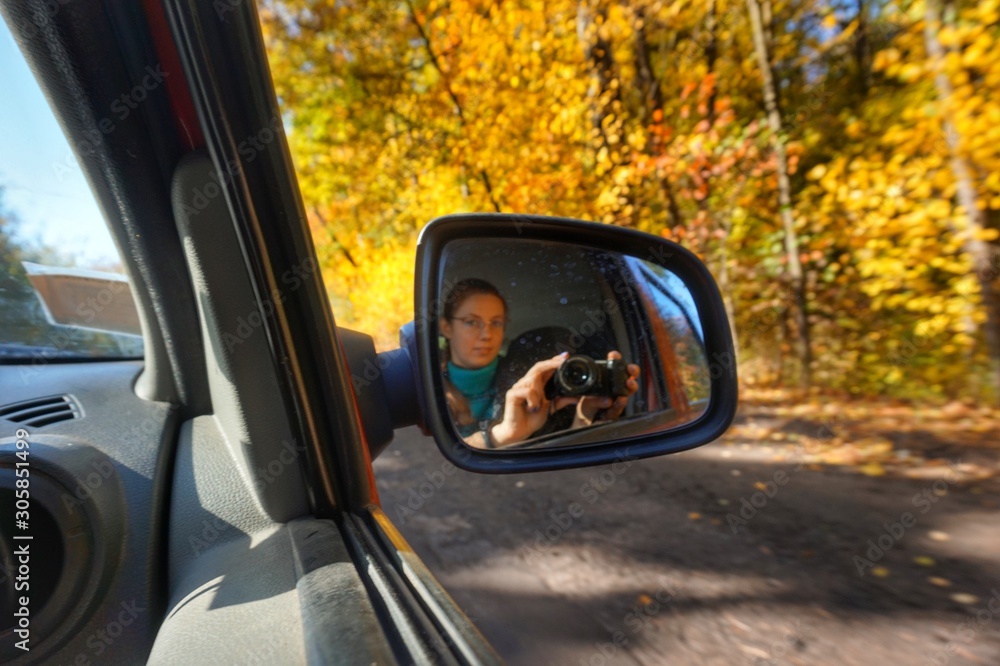 A girl photographs the road in the mirror of a car driving.