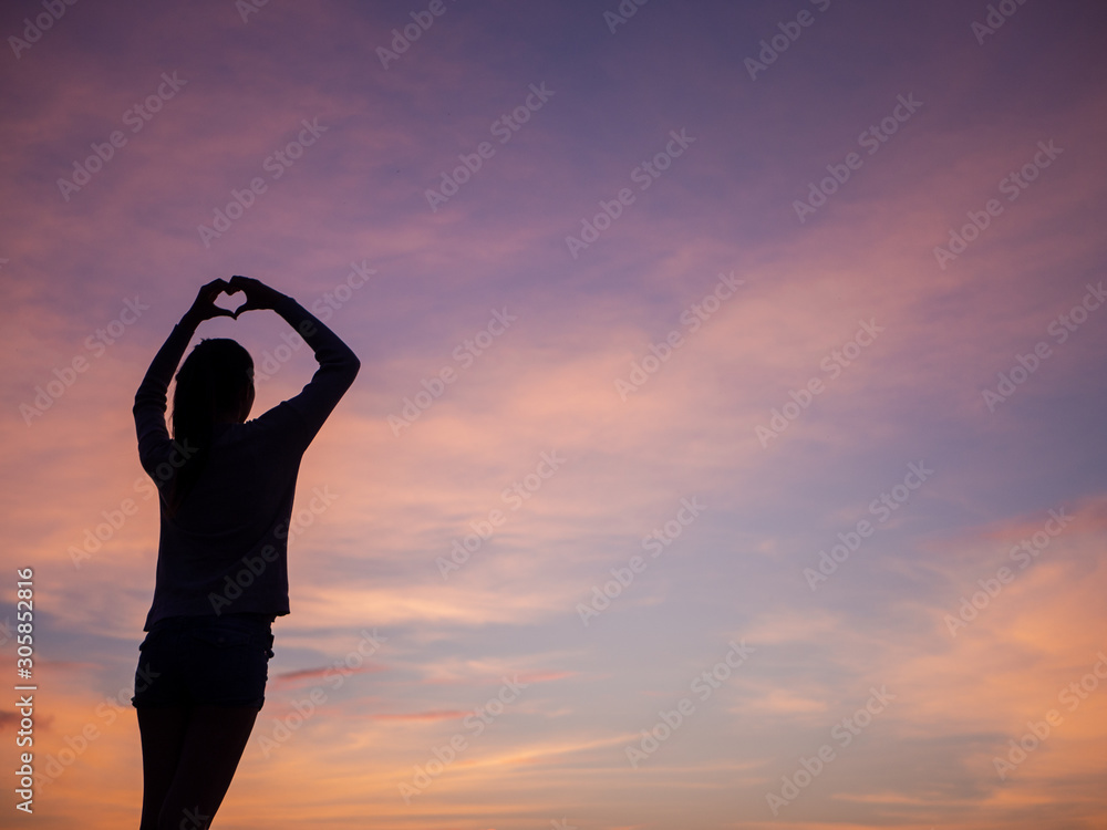 Young woman making heart shape at sunset 