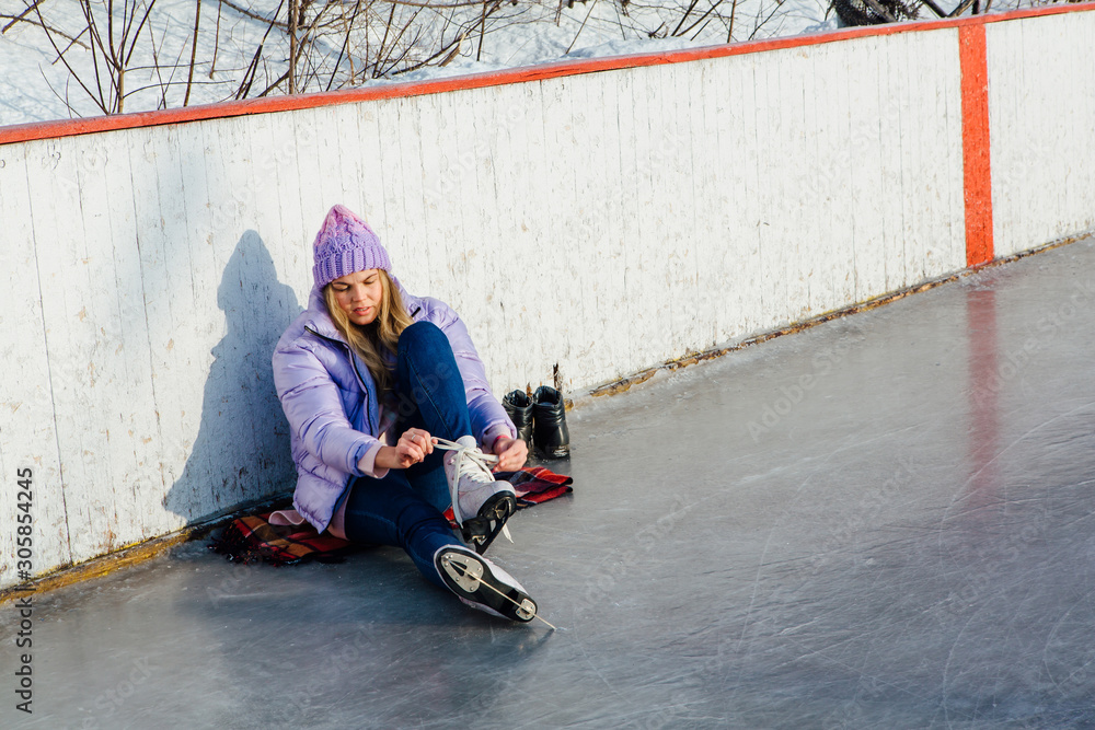 Lovely young woman sitting on ice ring and tieing shoelaces Lovely young woman sitting on ice ring and tieing shoelaces