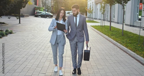 Caucasian businesswoman walking the street and demonsrating to her male colleague official numbers in documents and new contract. photo