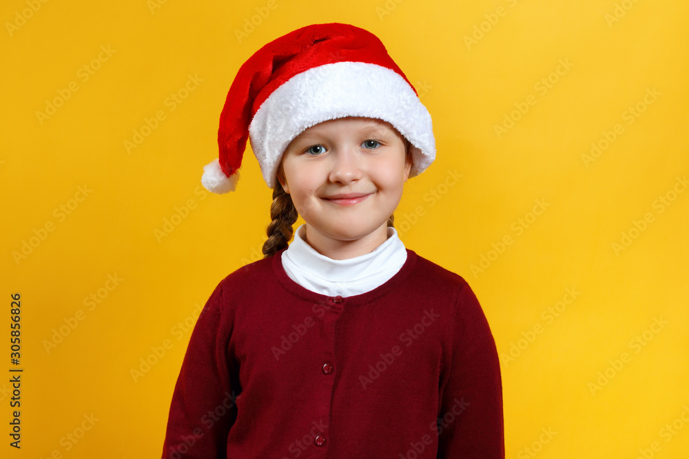 Christmas and New Year concept. Portrait of a cute adorable child in a Santa Claus hat. Little girl close-up on a yellow background Christmas and New Year concept. Portrait of a cute adorable child in a Santa Claus hat. Little girl close-up on a yellow background