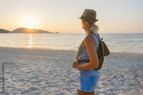 Young Woman With Backpack Standing On The Shore And Enjoying The Sunset Over The Sea