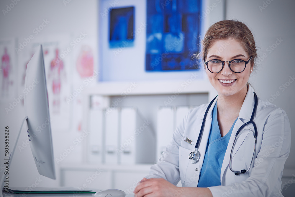 Beautiful young smiling female doctor sitting at the desk Beautiful young smiling female doctor sitting at the desk