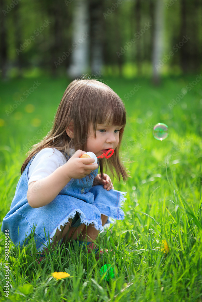 Little girl blows soap bubbles in the park in summer Little girl blows soap bubbles in the park in summer