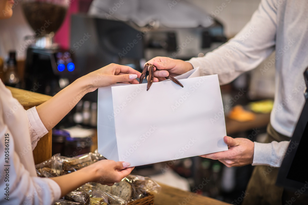 Close up of cashier passing bag with order to the customer - obrazy, fototapety, plakaty 