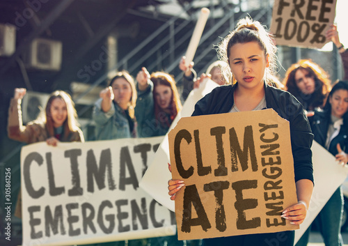 Young woman with poster in front of people protesting about climate changing on the street. Meeting about problem in ecology, environment, global warming, industrial influence, climate emergency. photo
